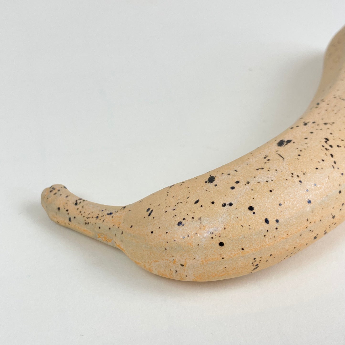 Orange ceramic banana with black speckles by Malwina Kleparska